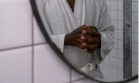 Tronco de homem negro, com mãos na frente e de roupão branco, se olhando ao espelho e pensando em o que é dismorfia sexual.