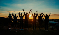 Grupo de pessoas de costas com mãos levantadas representando vários tipos de sexualidade e olhando o por do sol.