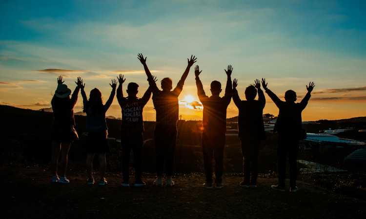 Grupo de pessoas de costas com mãos levantadas representando vários tipos de sexualidade e olhando o por do sol.