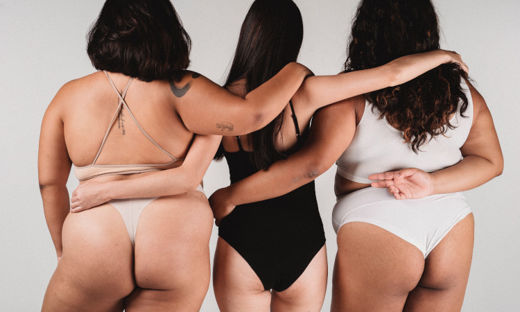 Três mulheres de costas - uma de fato de banho preto ao meio e mais magra, rodeada por duas mais gordinhas de fato de banho branco - ilustram os vários tipos de bumbum. 